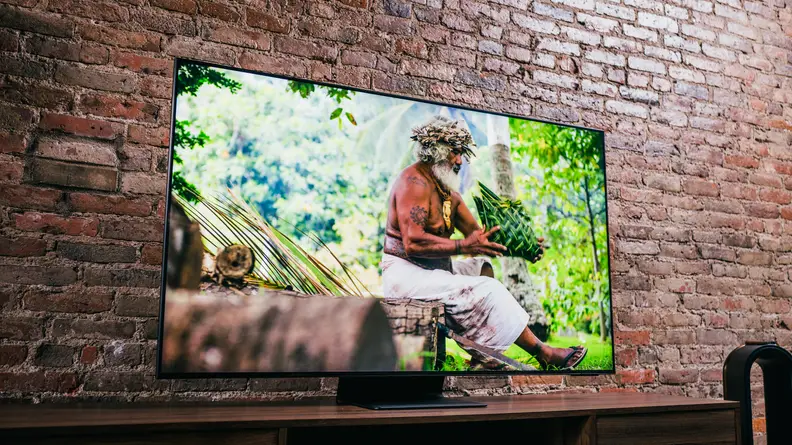 A muscular elder man sitting in a sunlit rainforest on the TV's screen