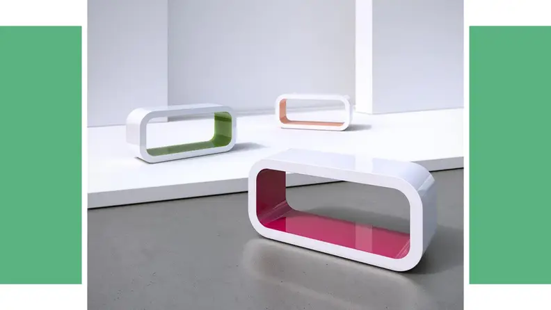 A uniquely-shaped coffee table in front of a green background.