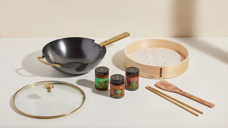 Carbon steel wok, accessories, and Fly by Jing sauces on a beige surface