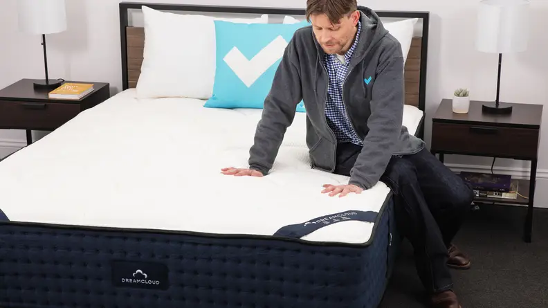 A person sitting on the DreamCloud mattress and pressing their hands into the surface.