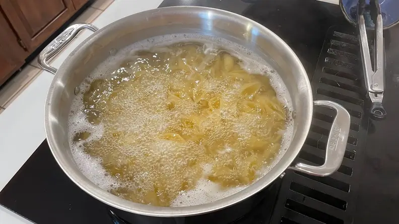 Pasta shells boiling in water inside of stainless steel pot.