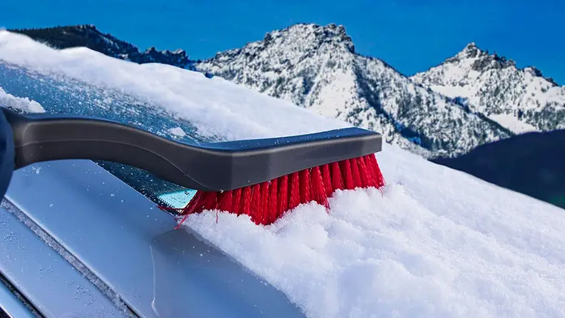 Someone using the Mallory snow brush to clean off a windshield.