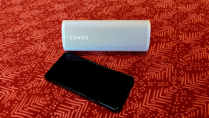 The white and tubular Sonos Roam on red table top next to a phone
