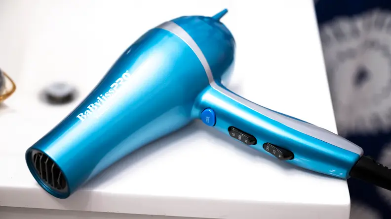 A metallic blue hair dryer sitting on the corner of a white sink.
