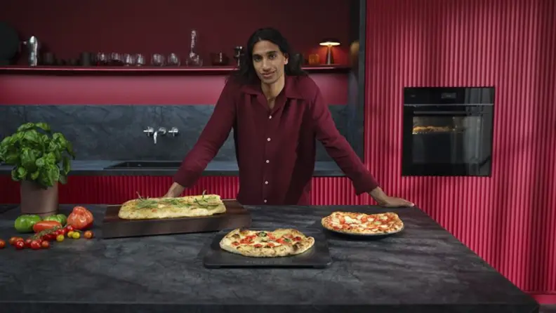 A man stands behind three pizzas