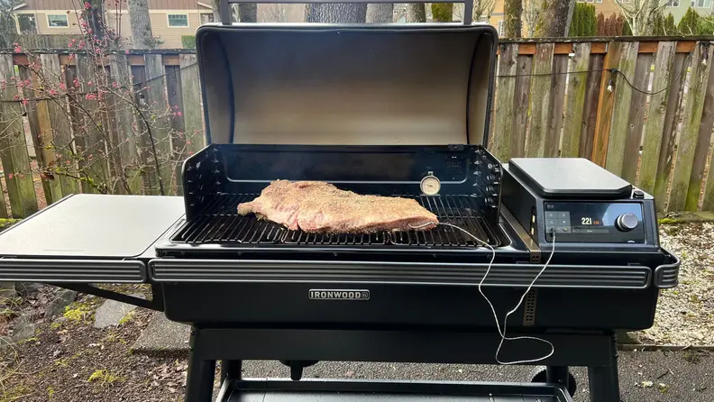 The Traeger Ironwood XL grill open with a piece of meat on top of the grill, cooking.