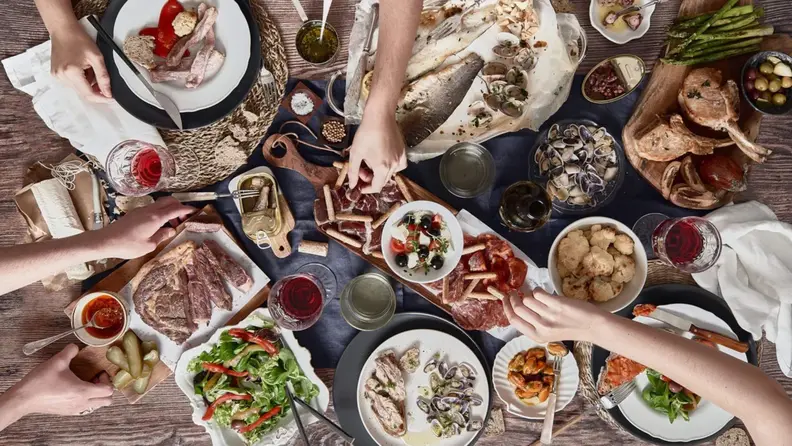Campo Grande variety of meats, veggies, and dips spread out on a table with people reaching to grab different foods.