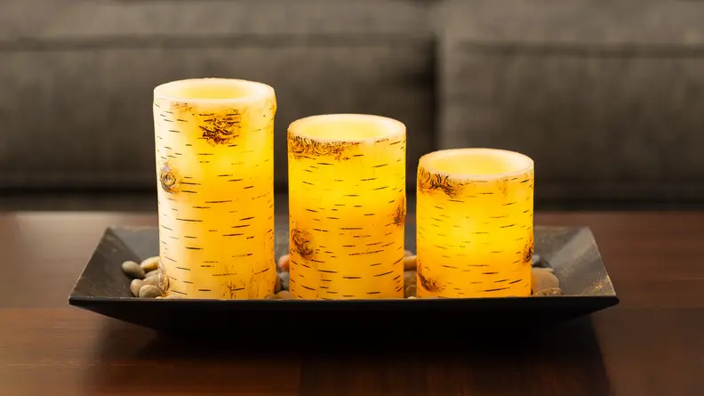 A trio of yellow Birch Bark Candlescape candles glow on a living-room table. They have no flame.