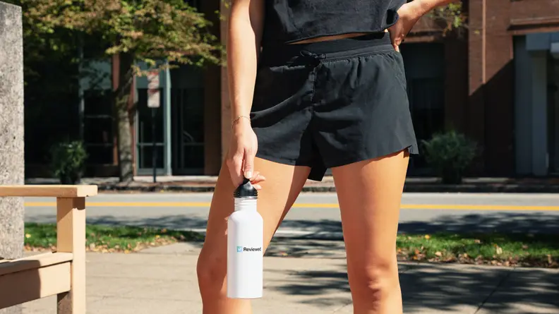 A person poses wearing black running shorts and holding a white water bottle.
