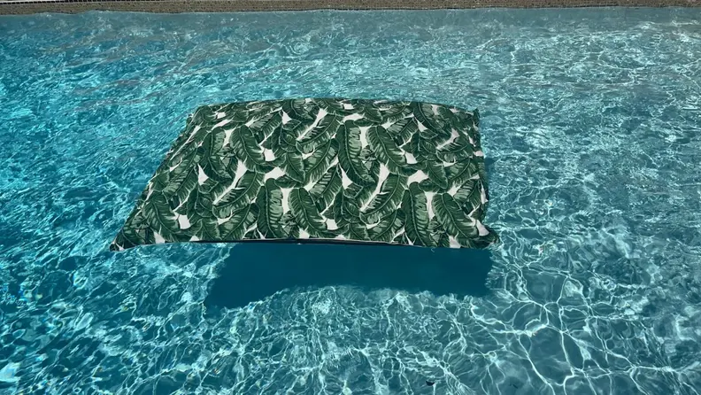 Empty Laze Pillow pool float in a fiddle leaf print floating in blue pool water.