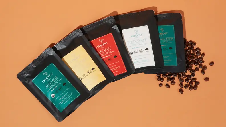 Five Lifeboost Coffee bags side-by-side, with coffee beans spread out on an orange background.