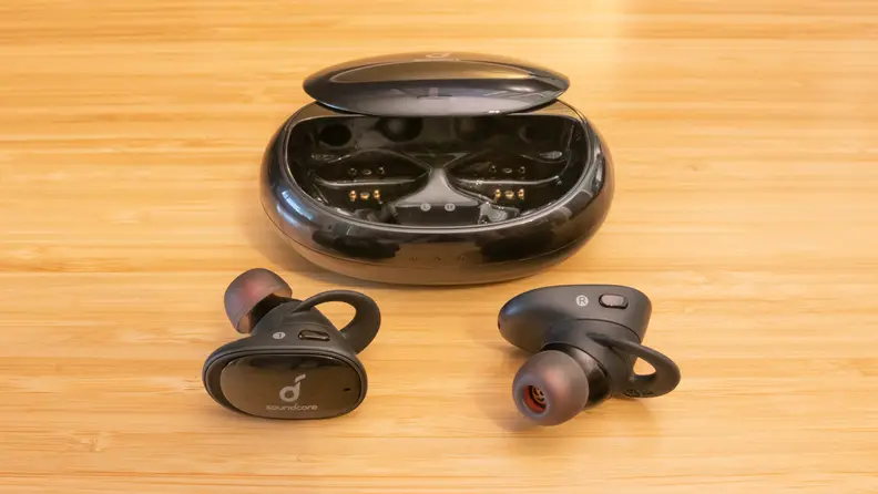 A pair of Anker Liberty earbuds and charging case on a brown table.