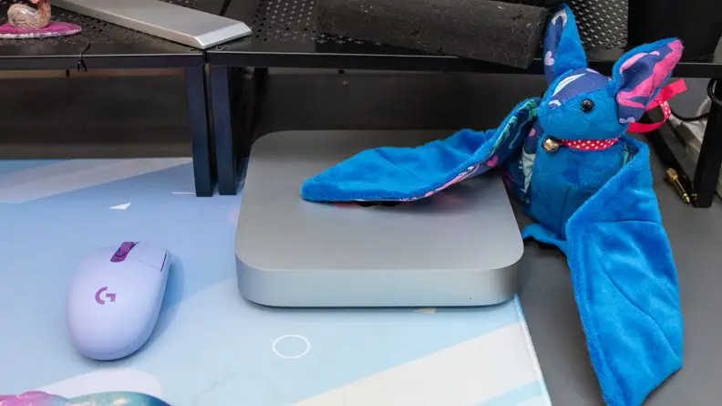 Apple Mac Mini M2 next to purple computer mouse and blue plush stuffed animal.