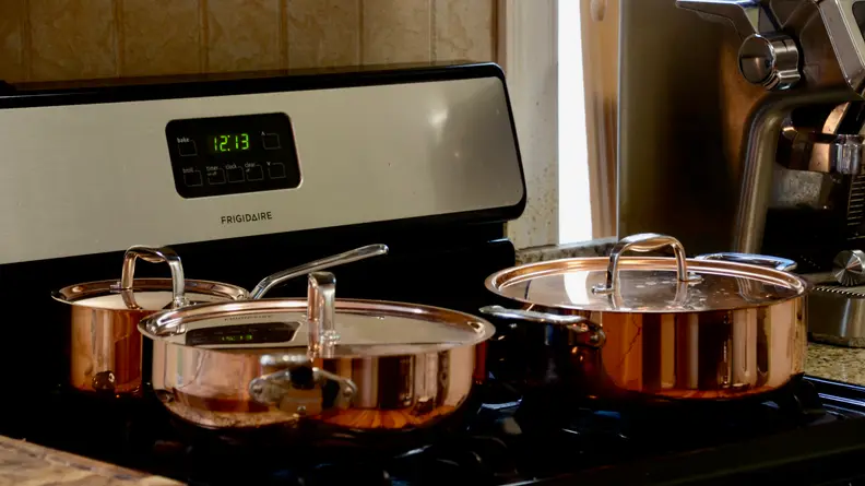 Copper cookware sits on a stovetop.