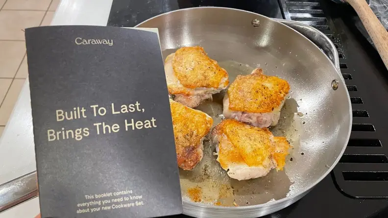 Four chicken thighs searing in a stainless steel pan next to instruction manual.