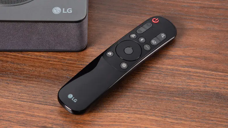 A remote control for an LG S80QY sits on a TV stand.