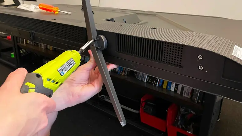 Person using neon green power drill to attach the TV leg stands on to the bottom of the TCL Q6 LED TV.