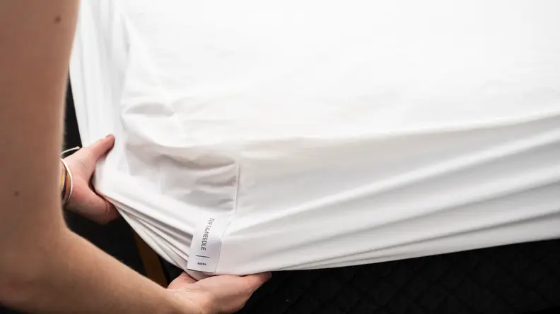 hands pull the Tuft & Needle mattress protector over the corner of a bed