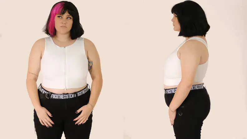A person with black and pink hair wearing a white zip-up binder and black pants, front and side profile.
