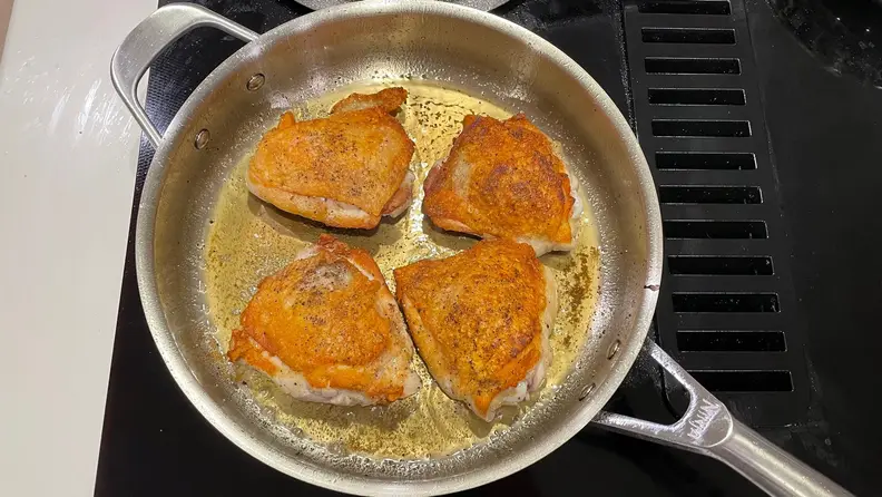 Four piece of meat being cooked in a stainless steel pan on a black stovetop.