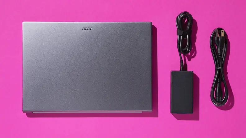 The Acer Swift X 14 laptop next to power cords on a pink background.