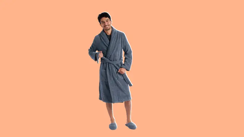 Person standing in a grey parachute bathrobe with grey slippers on a pink background