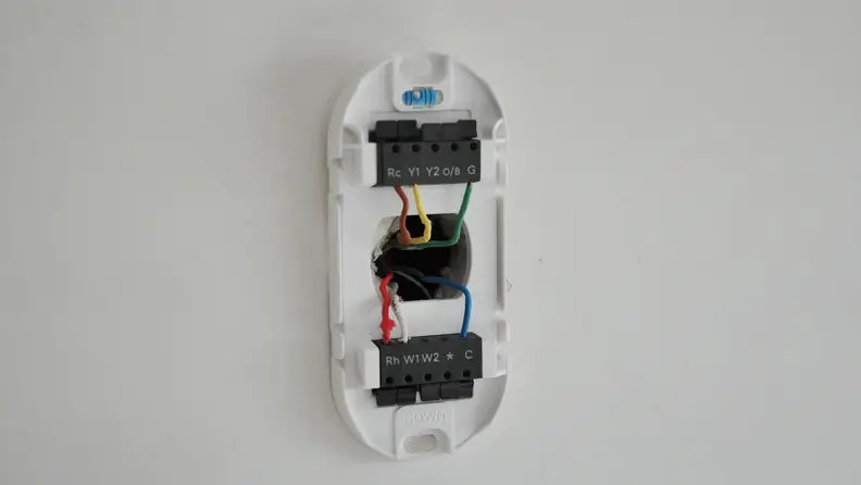 White Wyze Thermostat mounted on white wall. Cover removed to show wiring.