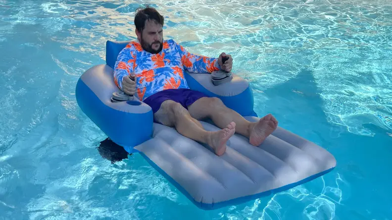 Person reclining on top of the PoolCandy Splash Runner motorized pool float in pool water outdoors.