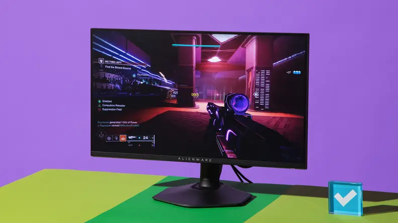 The Alienware AW2523HF gaming monitor on top of green and yellow surface in front of purple wall with display featuring interactive video game on screen.