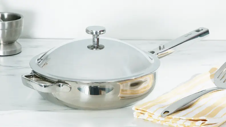 Titanium Always Pan Pro pan with lid attached next to spatula on top of a folded dishcloth.