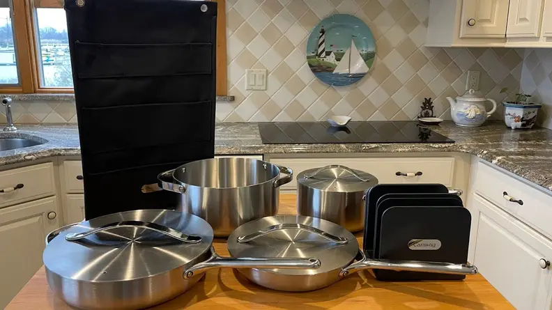 Caraway's stainless steel cookware set sitting on top of wooden island inside of modern kitchen.