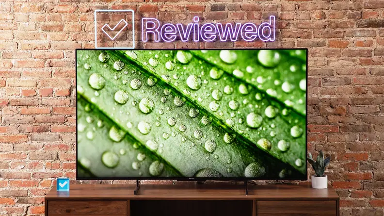 Hisense U7K Mini-LED TV sitting on top of wooden television stand in front of brick wall and Reviewed LED sign.