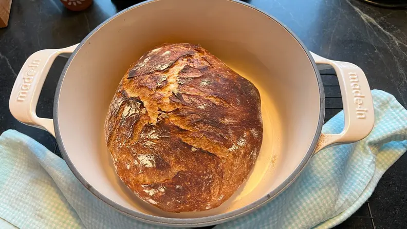 Round loaf of cooked break inside of the Made In Enameled Cast Iron Dutch Oven next to dish cloth.