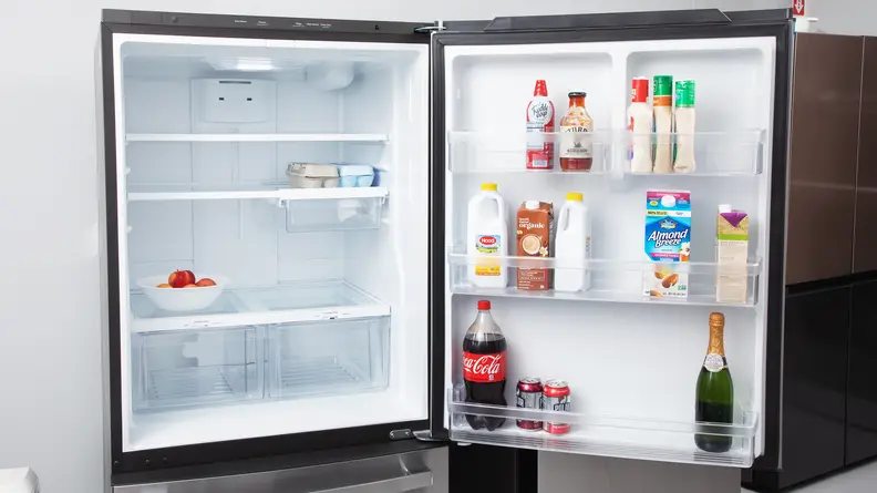 A refrigerator door stands open to show the useable space inside, with some food containers on the door
