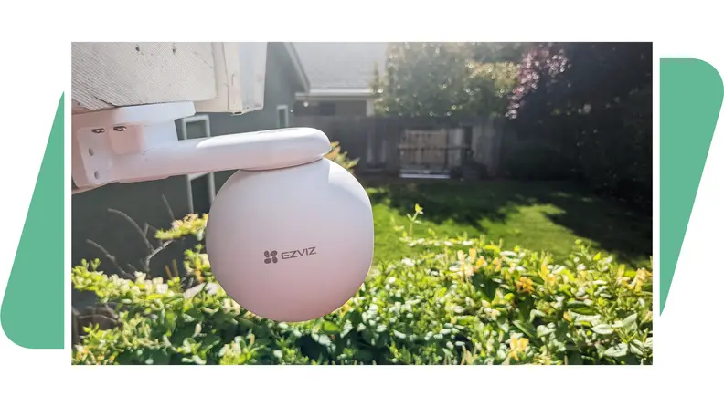 The  EzViz H8 Pro 3K outdoor camera, mounted to a house, facing a backyard with a green background.