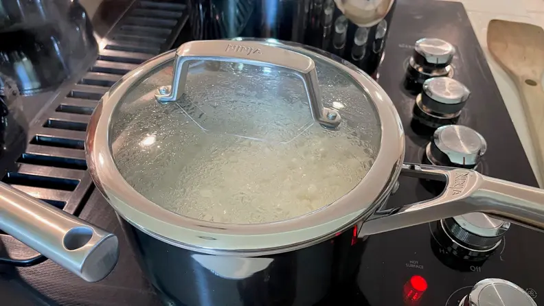 Rice being cooked inside a stainless steel pot, that's on top of a black stove top.