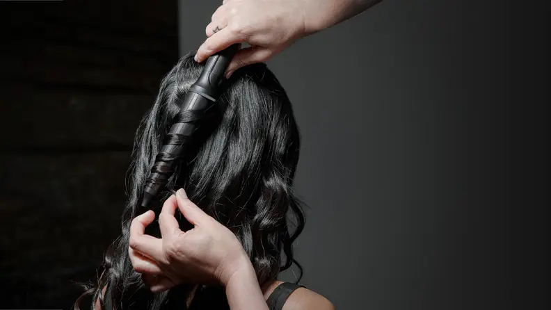Stylist uses GHD Curve Creative Curl Wand on woman with long black hair