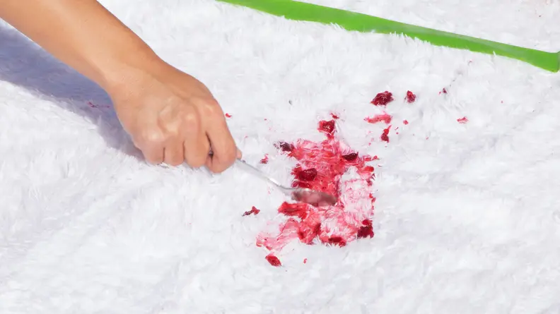 A person's hand spreads red cranberry sauce with a spoon on a white shag rug