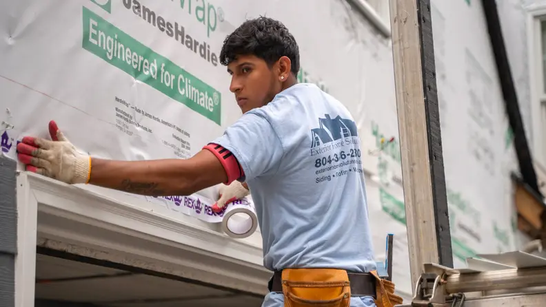A person installs siding to a home.