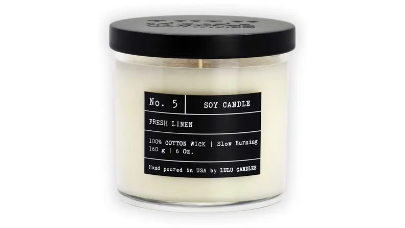 Product shot of white candle with black label and lid.