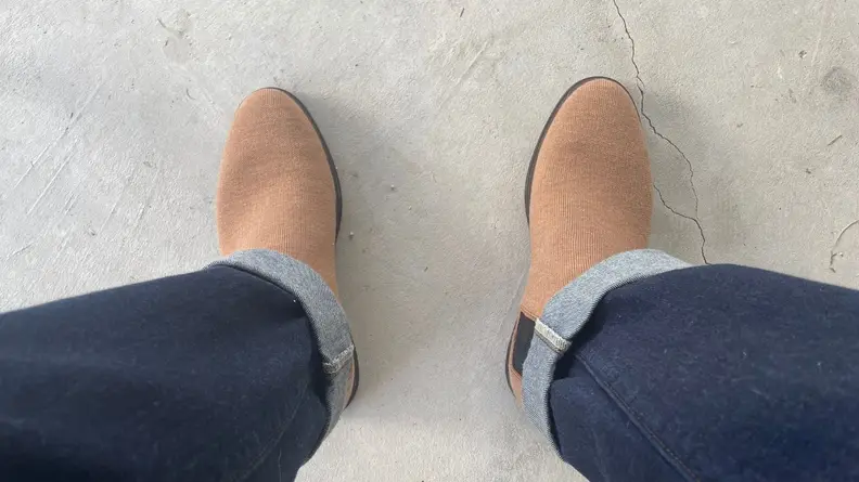 Person wearing jeans draped over bourbon colored Merino Chelsea Boots by Rothy's.