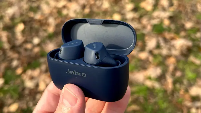 Jabra's navy Elite 4 Active earbuds are held in their case above yellow leaves.