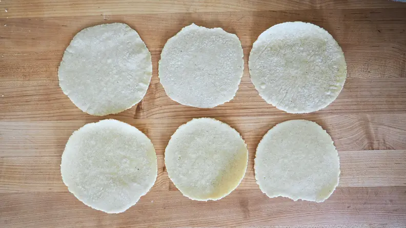 Six tortillas laid out in two rows on a wooden background.