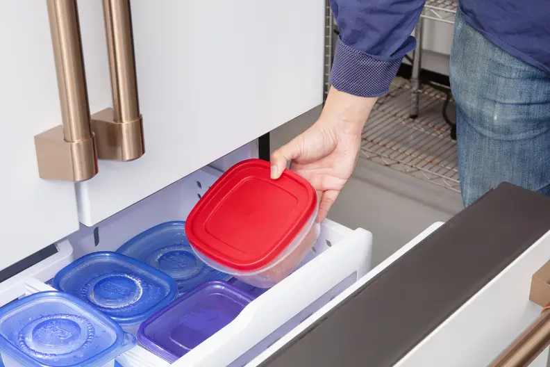 A person puts plastic containers in a freezer drawer