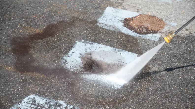 A pressure washer nozzle blasts water at a square painted on the ground.