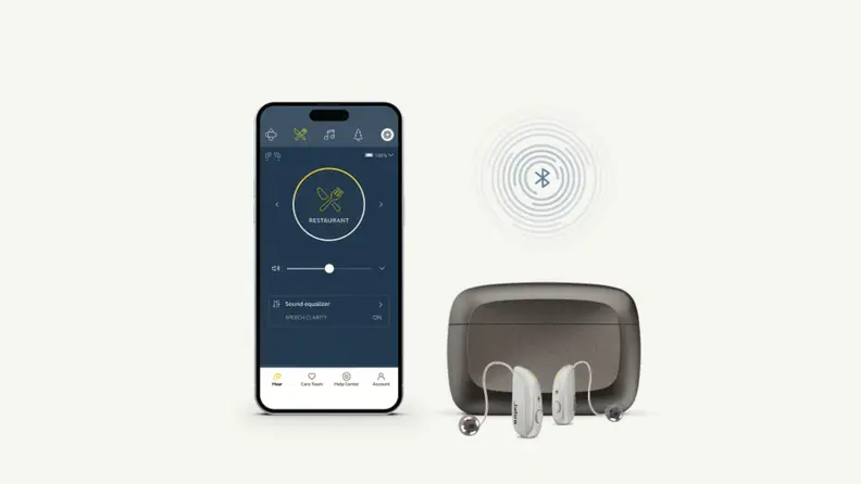 Beige background with phone open to Jabra Enhance 700 app next to a case and Jabra Enhance 700 hearing aids