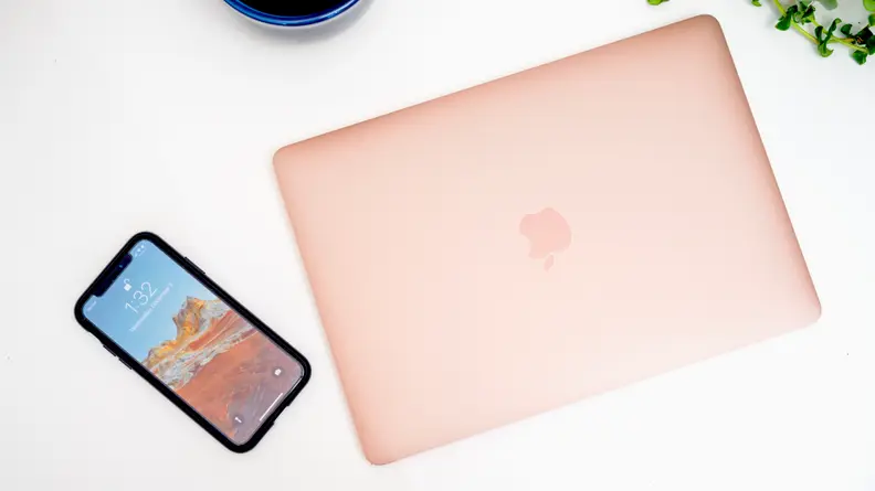 A rose-gold, or pink, MacBook Air. The laptop is closed; a smartphone lies beside it.