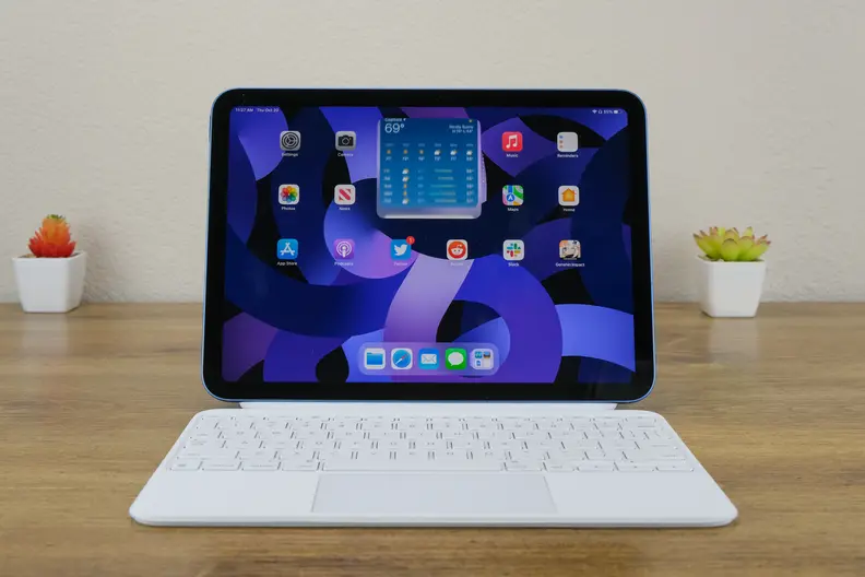 The Apple iPad 10 sits on a wooden desk with its white keyboard facing forward.