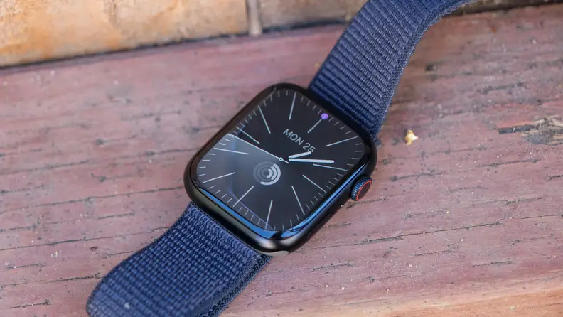 An Apple Watch sits on the railing of a backyard deck, on a sunny day.