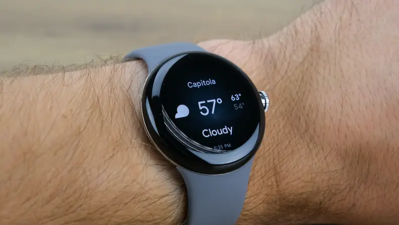 The Pixel Watch is shown on a wrist with a gray band and a circular black screen.